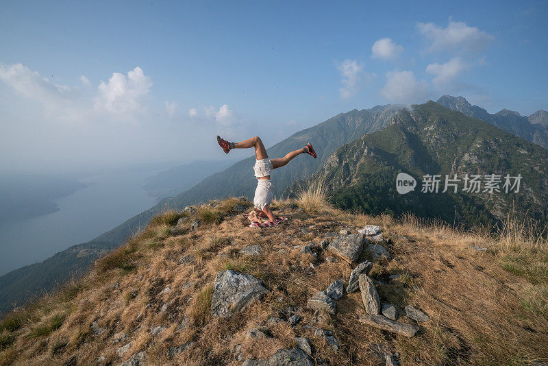 在一天的徒步旅行后，一名年轻女子在山顶上练习倒立瑜伽。人们健康旅行的生活理念