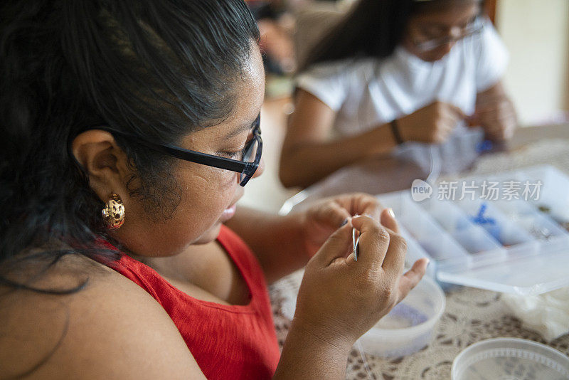 漂亮的身材积极的拉丁裔墨西哥妇女做工艺品，花哨的珠子，和她的女儿