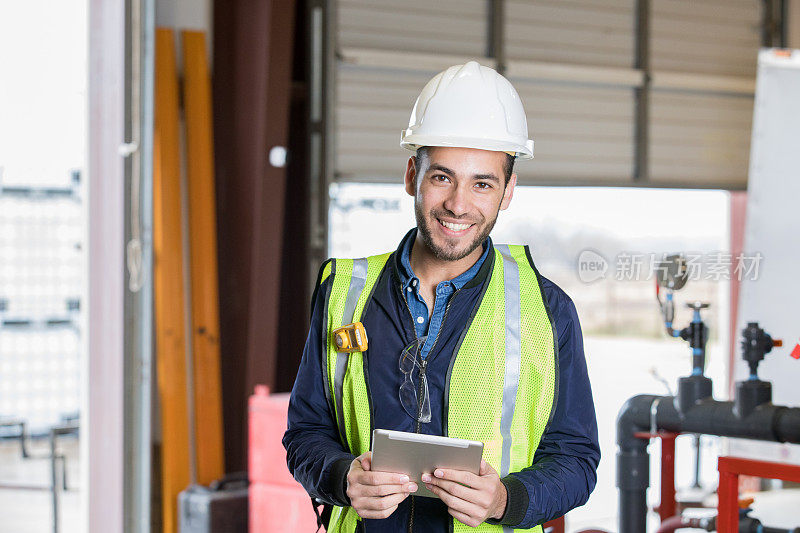 一名年轻的西班牙裔男子微笑着在石油和天然气行业工作，并使用数字平板电脑