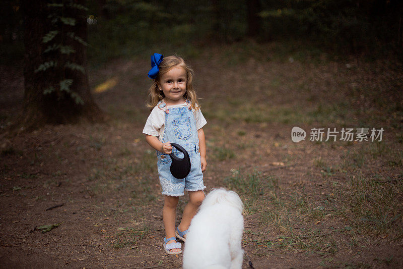 小女孩带着她的小狗在森林里散步