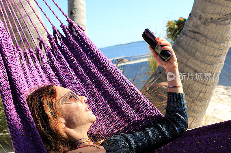 美丽的女人自拍和放松在热带沙滩上的吊床