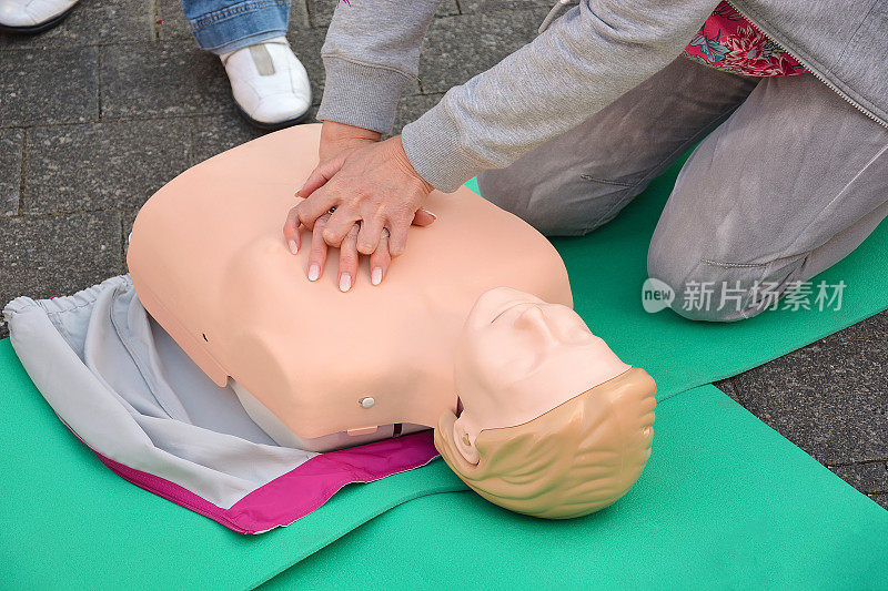 在街上进行心肺复苏急救假人训练。一个女人跪在一个人体模型旁边。
