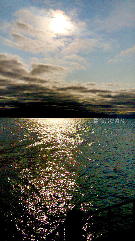 太阳的形象隐藏在暴风雨的乌云天空与阳光反射在平静涟漪的海面