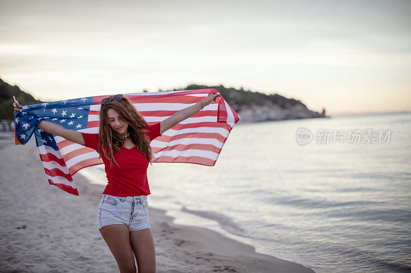 海滩上拿着美国国旗的年轻女子