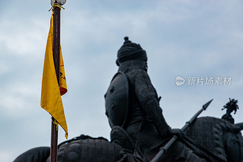 一面黄色旗帜，背景是普拉塔普王公的青铜雕像。