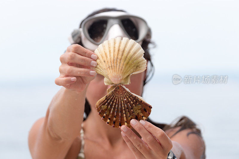 一个女人在海滩上拿着两个贝壳