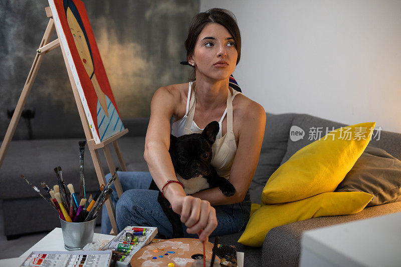 一个漂亮的年轻画家在画着一只小狗在她腿上