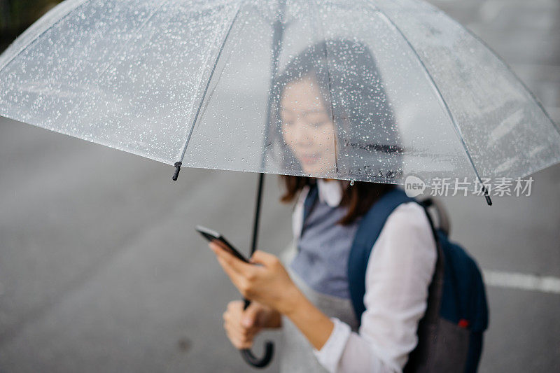 年轻的亚洲女人在雨天使用电话