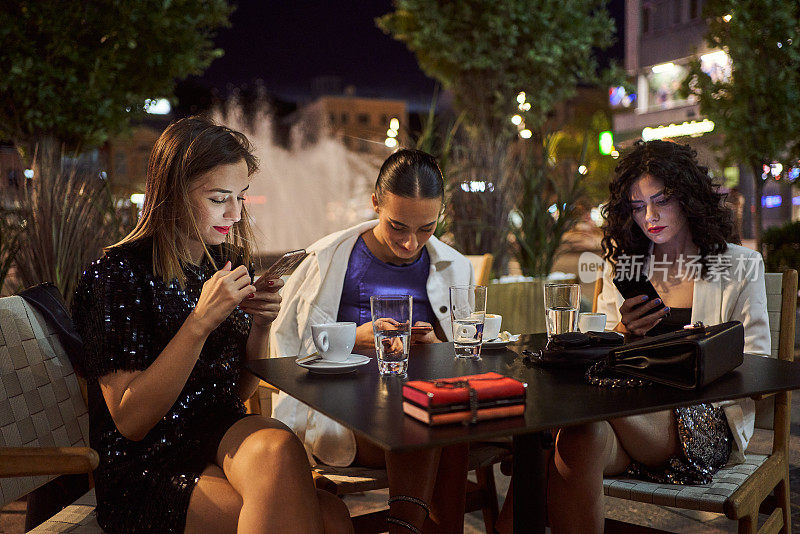 年轻女性在晚上外出时彼此分开使用手机