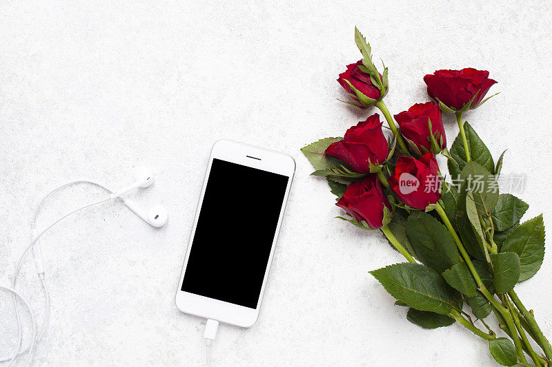 俯视图手机模板和耳机与玫瑰在一个轻纹理背景与复制空间