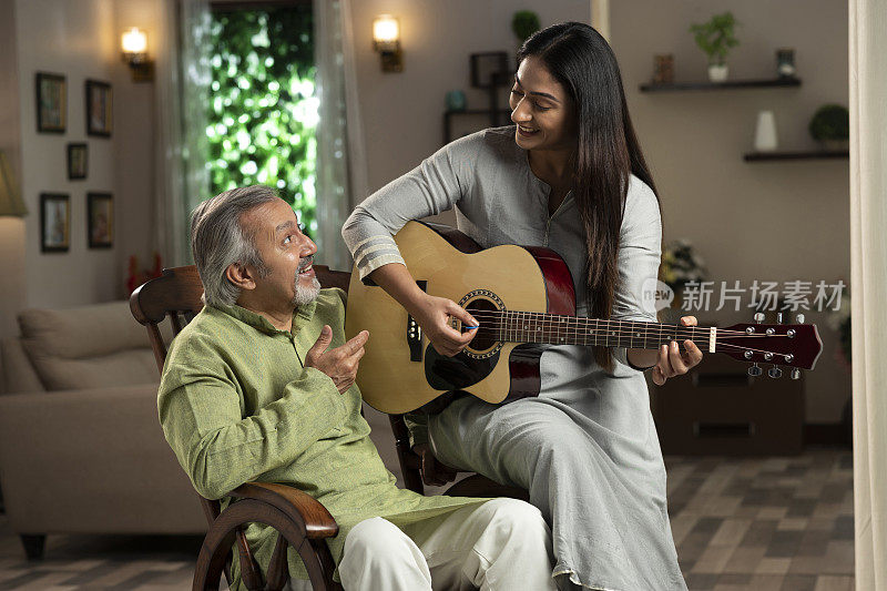 一个年轻女人和她成熟的父亲坐在摇椅上的肖像。她在家里弹吉他:-库存照片