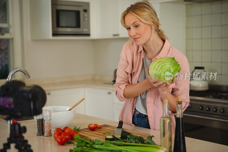 微笑的白人妇女在厨房拿着生菜，看着镜头，做烹饪视频