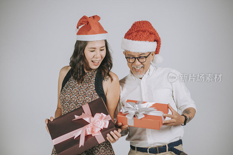 亚洲华人成熟夫妇有有趣的圣诞派对礼物交换工作室拍摄与灰色背景