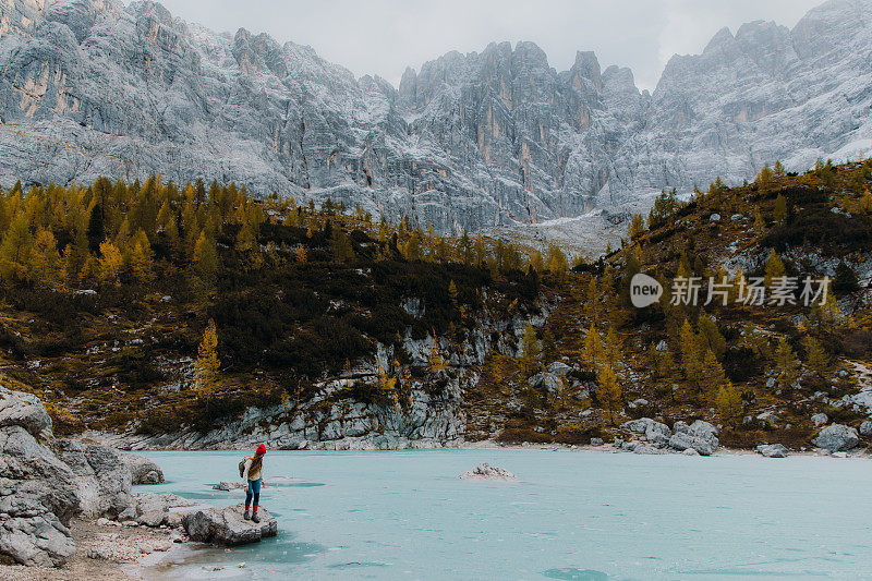 女旅行者呆在岩石上，欣赏阿尔卑斯山上冰封的高山湖泊的风景