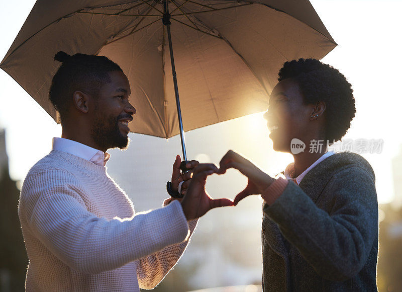 一个下雨天，一个年轻的男人和女人一起站在雨伞下，用手做了一个心形