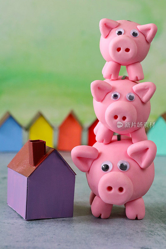 三个模型猪的形象除了紫色，模型纸板房子，排彩色的海滩小屋，重点前景，斑驳的绿色背景，家庭财务，房地产和假日储蓄概念