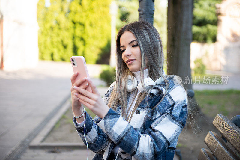 快乐的年轻女子走在城市的街道上，用她的智能手机