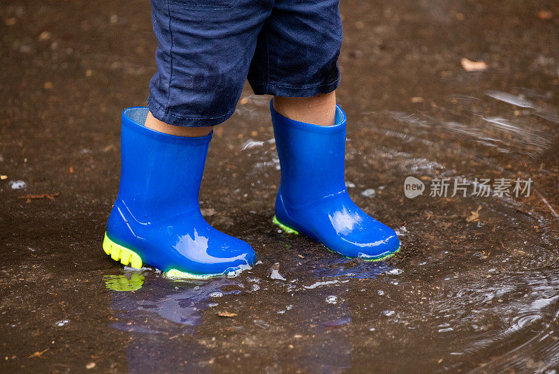 一个穿着蓝色胶靴的小孩在雨天踩在水坑里