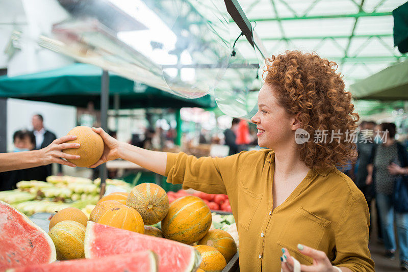 美丽的红发女人在市场上购买新鲜水果