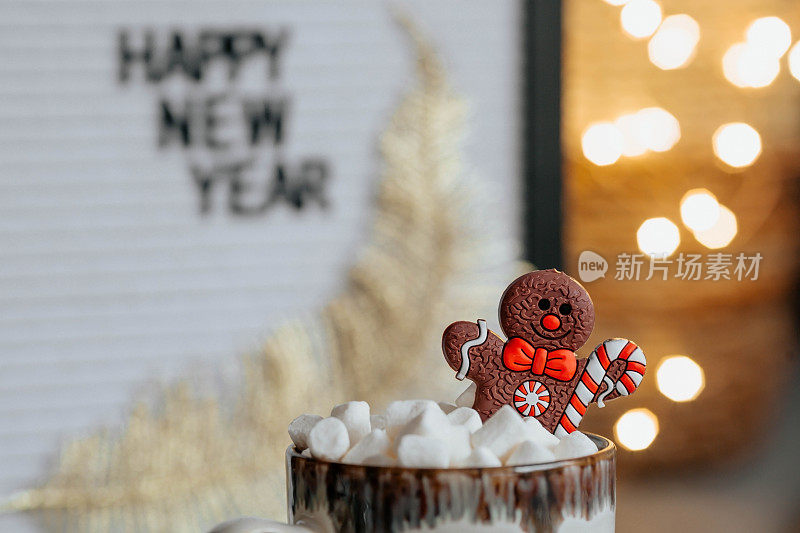 一个写着“新年快乐”的牌子，一个以漂亮的黄色小盆栽为背景的杯子，上面放着热可可、棉花糖和姜饼人。一个温馨的圣诞和冬季假期的概念。