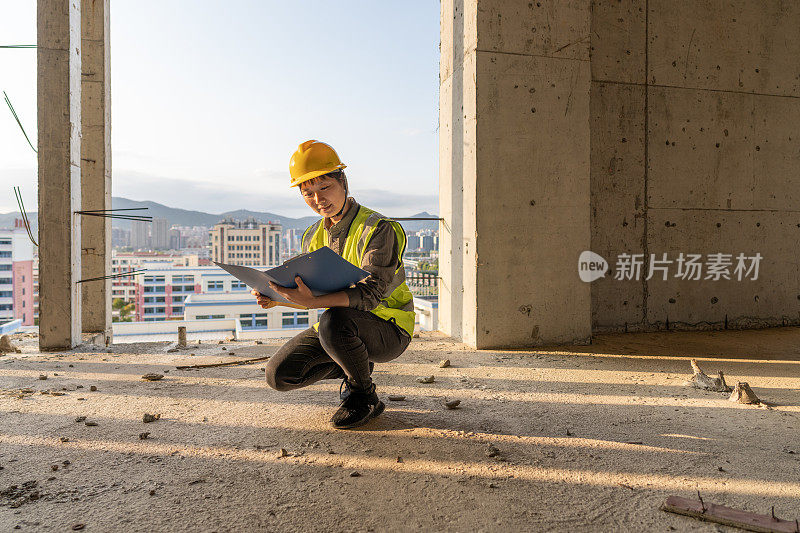 一位亚裔女工程师蹲在建筑工地的地板上看图纸