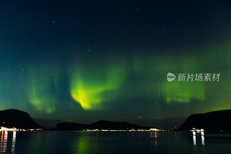 风景秀丽的北极光在峡湾和发光的城镇在挪威