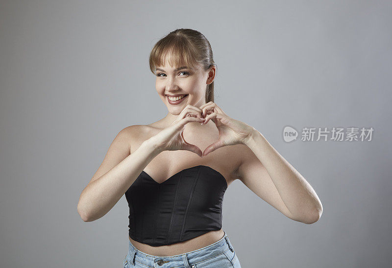 带着刘海微笑的年轻女子用手做心形符号。