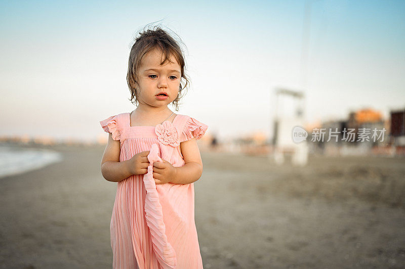 海滩上穿着粉红色裙子的沉思的女婴