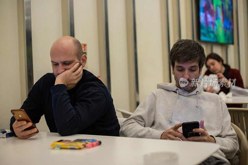 两个年轻人坐在一起，每个人都在玩手机