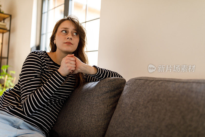 焦虑的年轻女子坐在沙发上，沉思着，掰着指关节