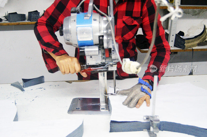 纺织工人在纺织厂使用切割机或直刀切割机，纺织切割机是一种用于切割织物的大型机器，并佩戴链手套以保护双手