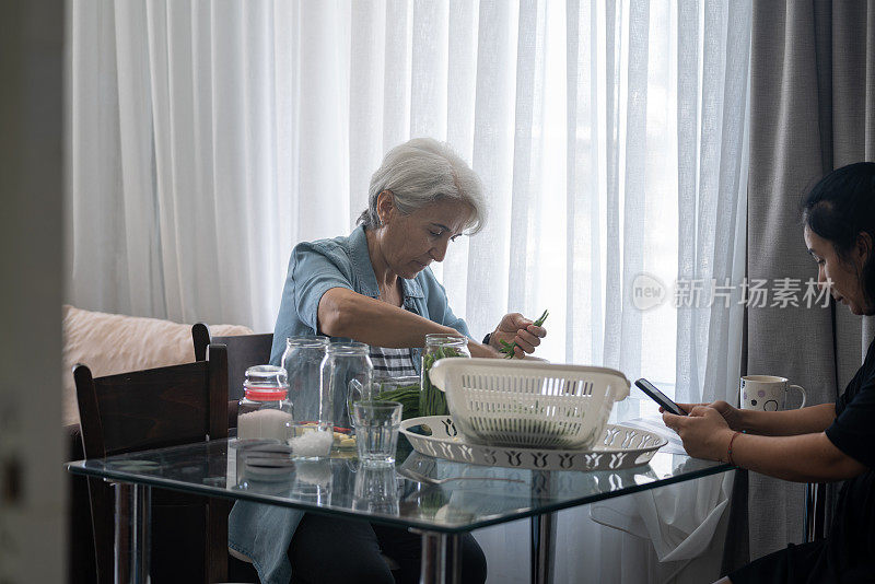 老年妇女和成熟的成年朋友准备青豆调味料的照片