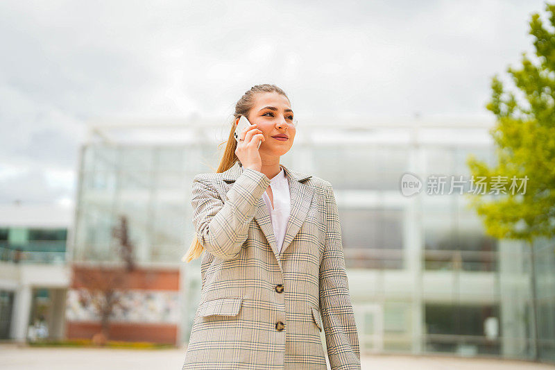 年轻漂亮的棕发女商人在商务中心的花园里打电话