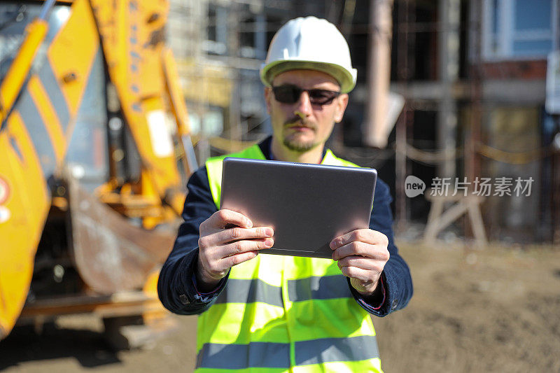 男建筑师在工地使用数码平板电脑，他穿着防护背心和头盔