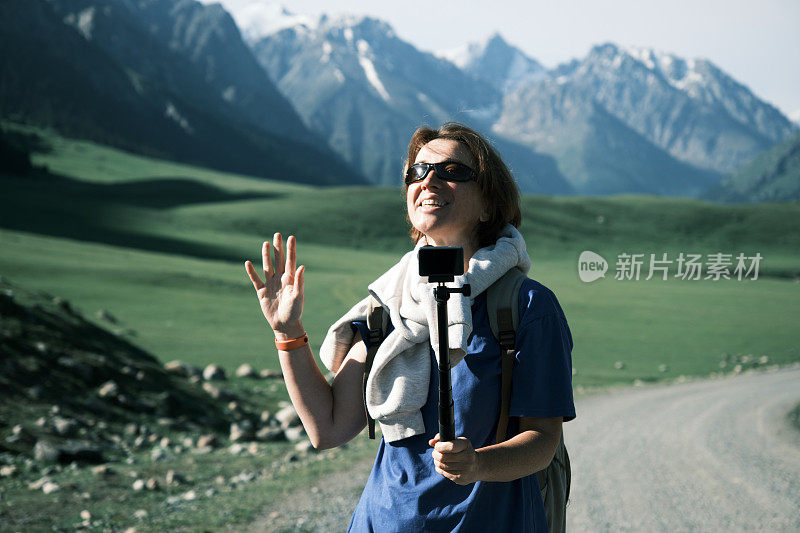 开朗的成熟女性背包客在天山的高地路上拍摄视频