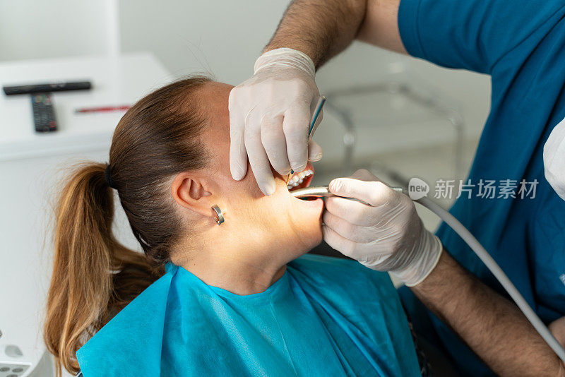 牙医在牙科诊所的牙科椅上给女病人钻牙。