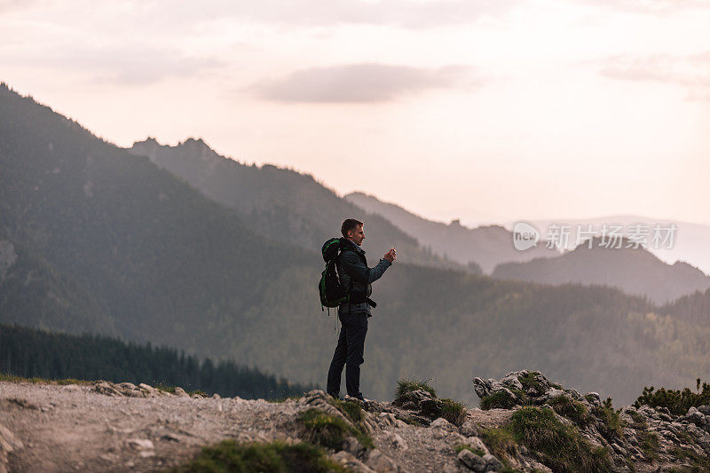 男人的男性肖像，在山中旅行。穿着保暖运动服在户外徒步旅行的人。真实人物的生活方式摄影，旅游理念。这家伙是个背包客，背包里装着旅游装备，用手机拍风景。