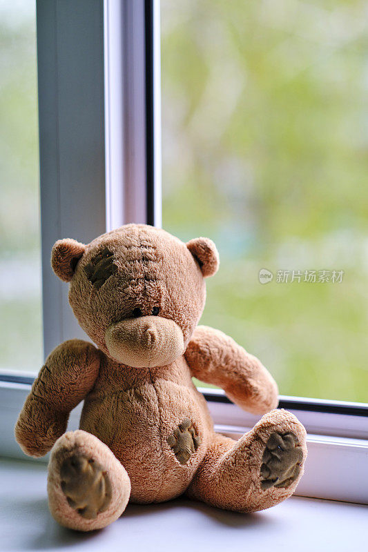 小熊的毛绒玩具坐在开着的窗户边。与孩子的概念事故。