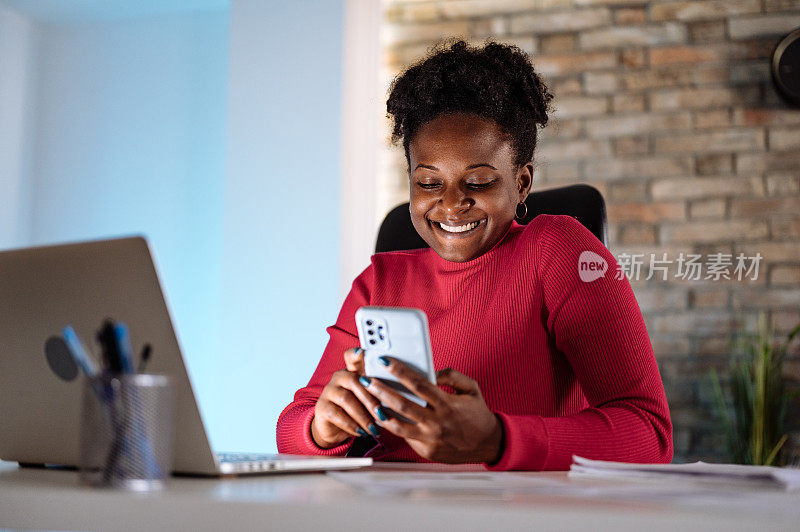 非裔加勒比女商人在办公室工作到很晚，使用笔记本电脑和智能手机进行交流