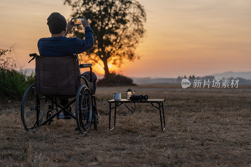 一个人坐在轮椅上，看着第一个金色的日出。残疾人有希望。