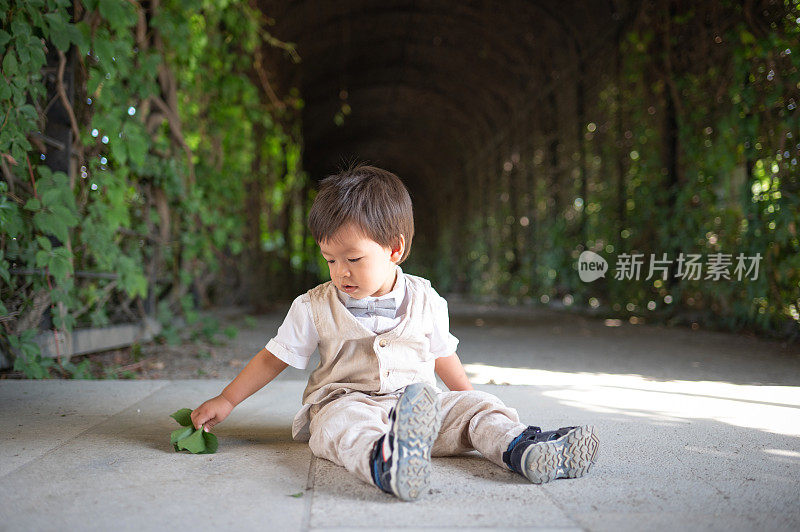 一个多种族的幼童心满意足地坐在公园的小路上