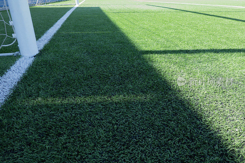 足球场上的人造草皮。部分足球球门和运动场上的绿色合成草，球门网的阴影