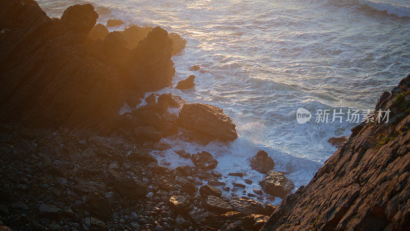 波浪飞溅悬崖边缘在金色的光。海岸上的岩石在宁静的日落中大海