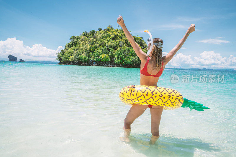 快乐的年轻女人在海滩度假探索热带岛屿-充气菠萝和浮潜装备