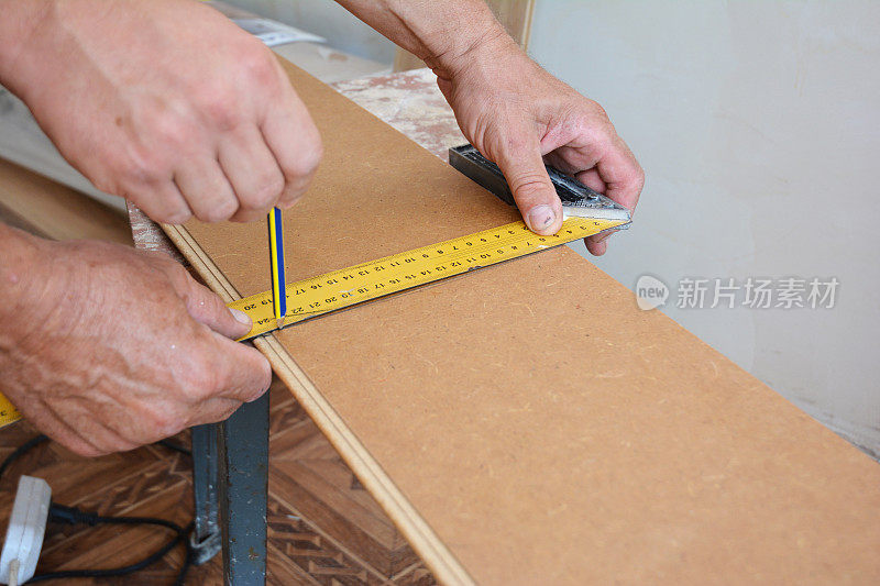 安装木质强化地板及切割前测量强化板的工人。