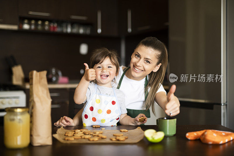 快乐的家庭与烤饼干，母亲和女儿有乐趣和吃新鲜热饼干