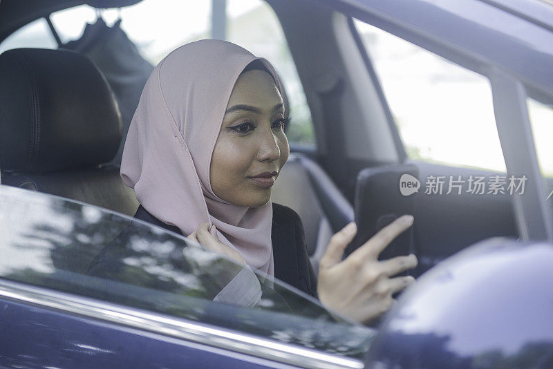 亚洲穆斯林女性司机在汽车中使用智能手机
