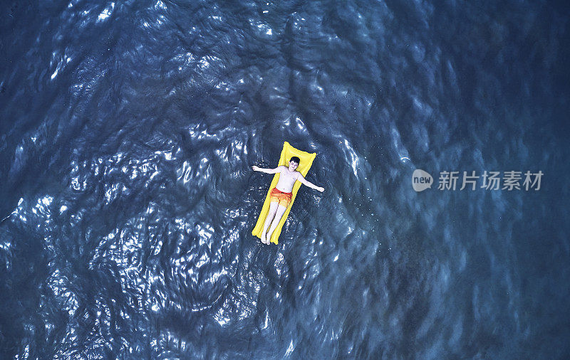 鸟瞰图上的小男孩游泳在黄色游泳环在透明的绿松石海在帕塔拉