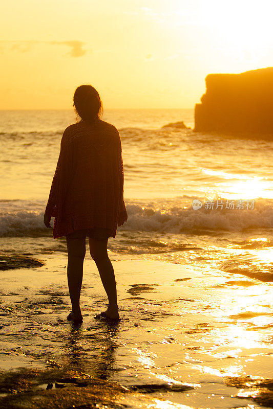 亚洲女人站在海边的海滩在日落