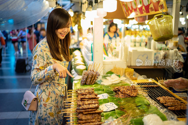 亚洲妇女从街头小贩买泰式猪肉烧烤棒